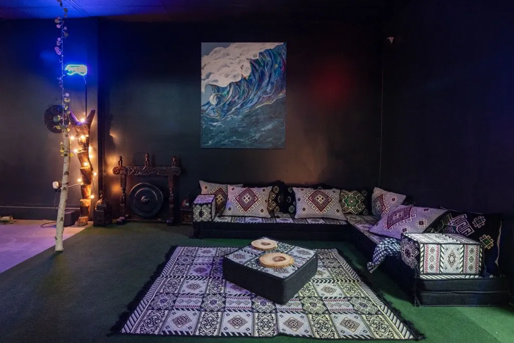 Patterned floor cushions and low tables sit beneath wave artwork beside a gong inside Tribe Tea Lounge
