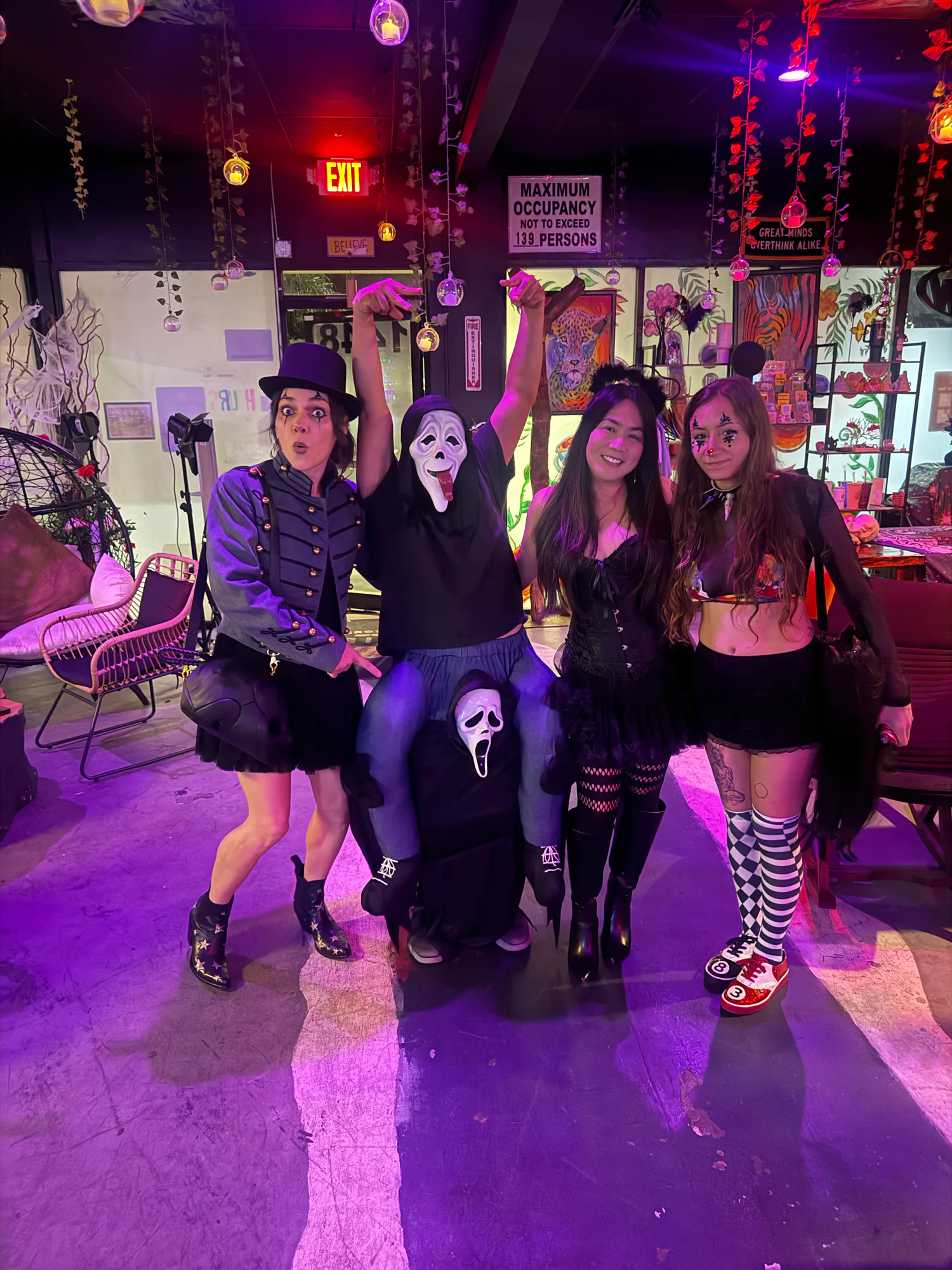 Four people in costumes pose together beneath hanging flowers at Tribe Tea Lounge