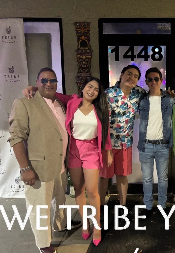 Four people stand arm in arm beside Tribe Tea Lounge’s entrance and branded backdrop