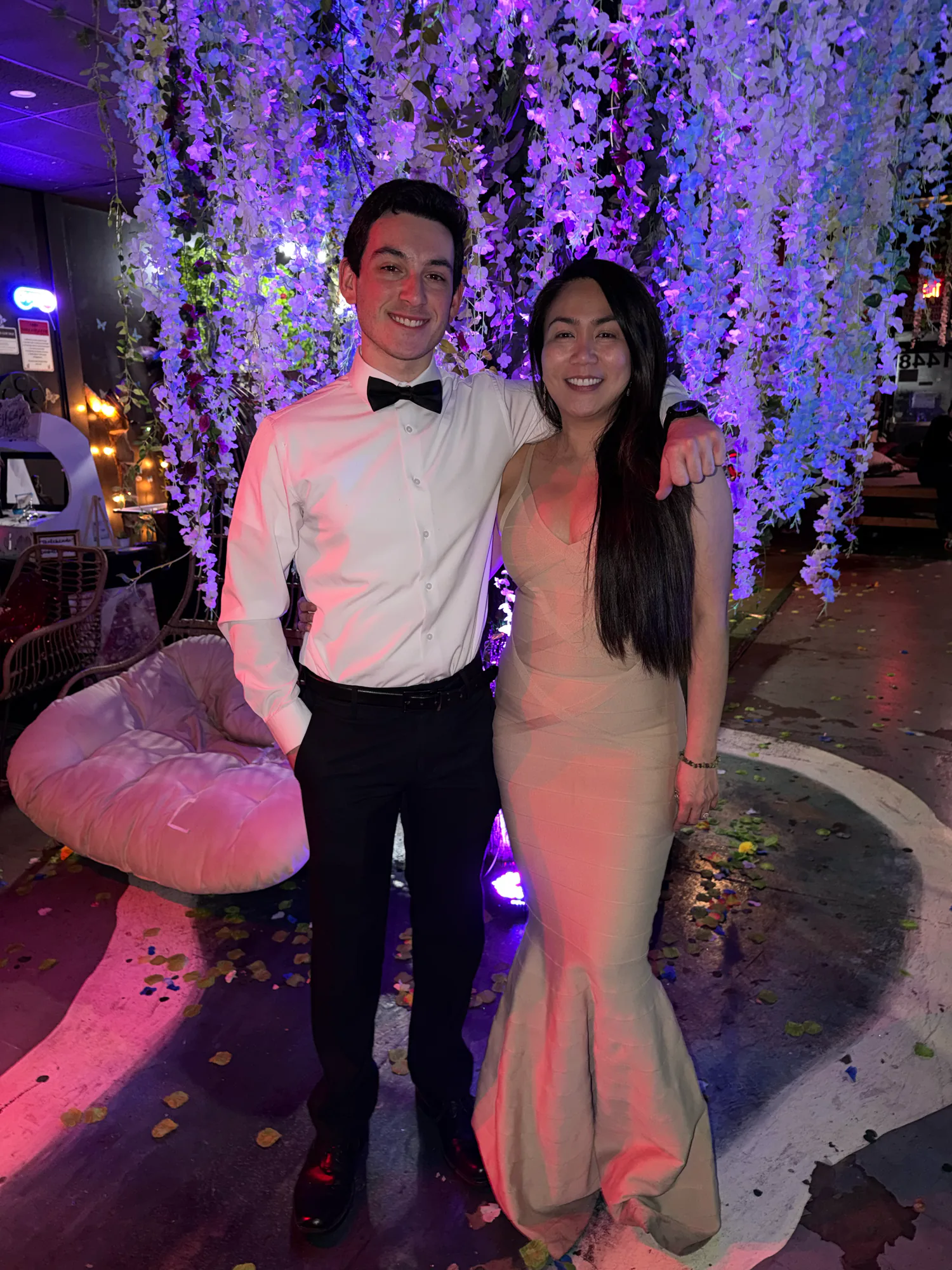 Two people dressed for an evening at Tribe Tea Lounge pose beneath its hanging flowers