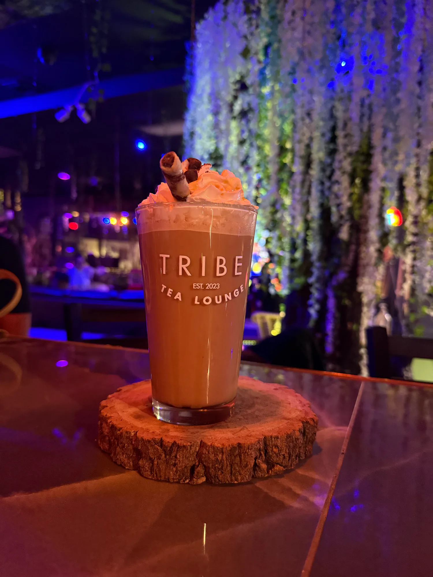 A Tribe-branded drink is topped with whipped cream, a rolled wafer, and chocolate pieces