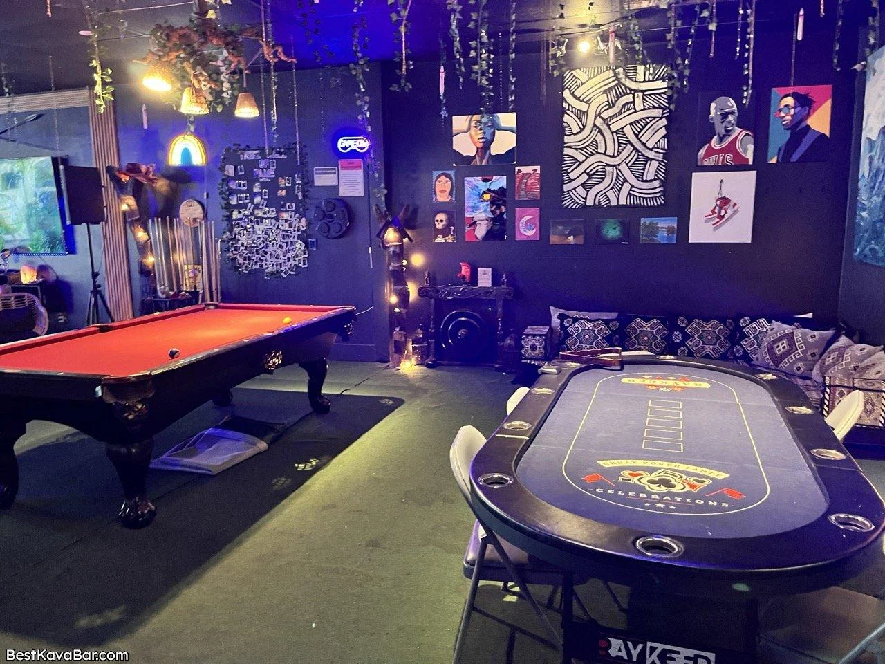 A red-felt pool table and a poker-style table sit beneath artwork and hanging lights at Tribe Tea Lounge
