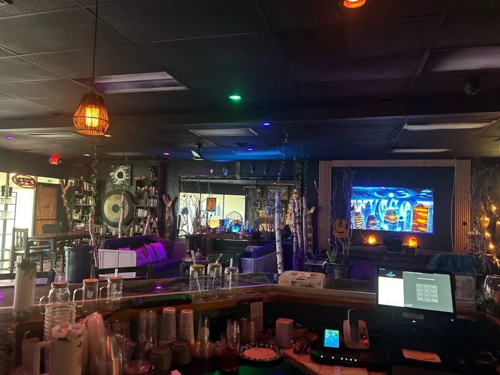 A view from Tribe Tea Lounge’s counter shows bottles, hanging lamps, seating, and a glowing wall display