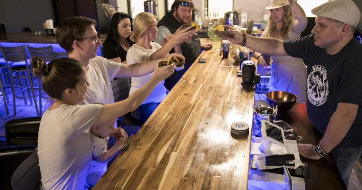 Kava bar team and guests raising traditional shells together across a wooden bar